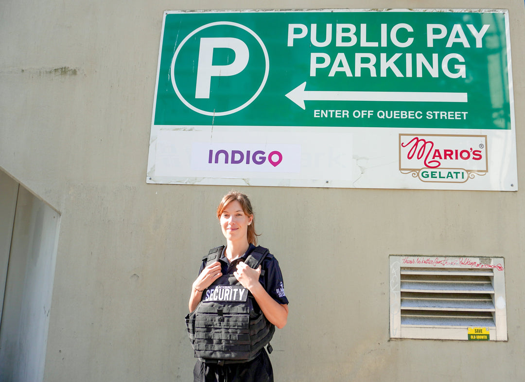 Uniformed Blackbird security guard standing in front of Public Pay Parking lot sign