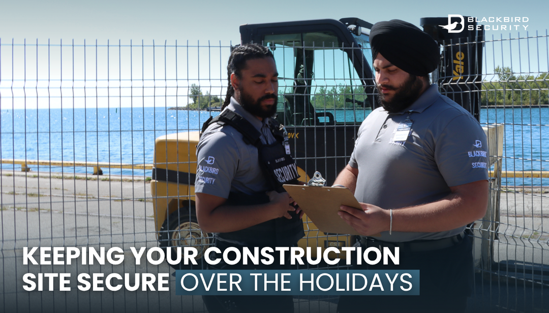 Two Blackbird Security construction site security guards stand in front of a fence looking at a clipboard.