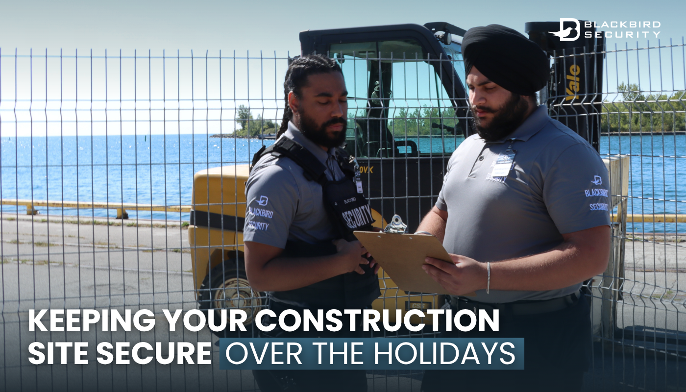 Two Blackbird Security construction site security guards stand in front of a fence looking at a clipboard.