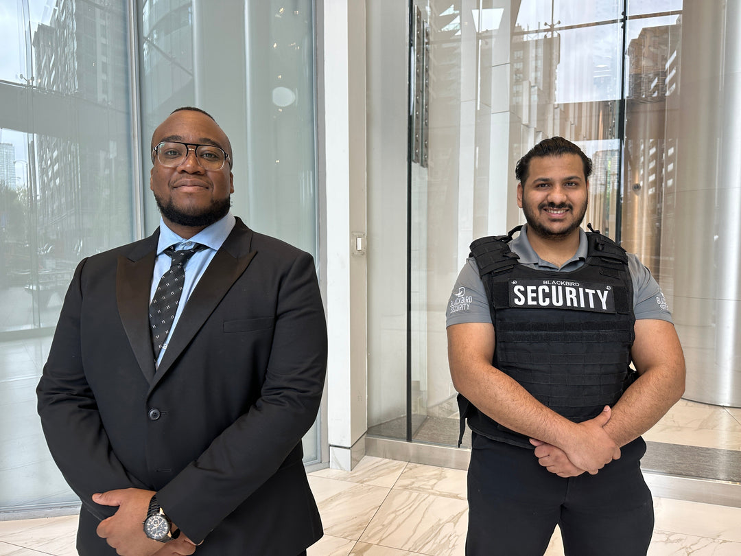 Uniformed Blackbird security guard and a suit and tie security guard stand in front of a condominium building entrance 