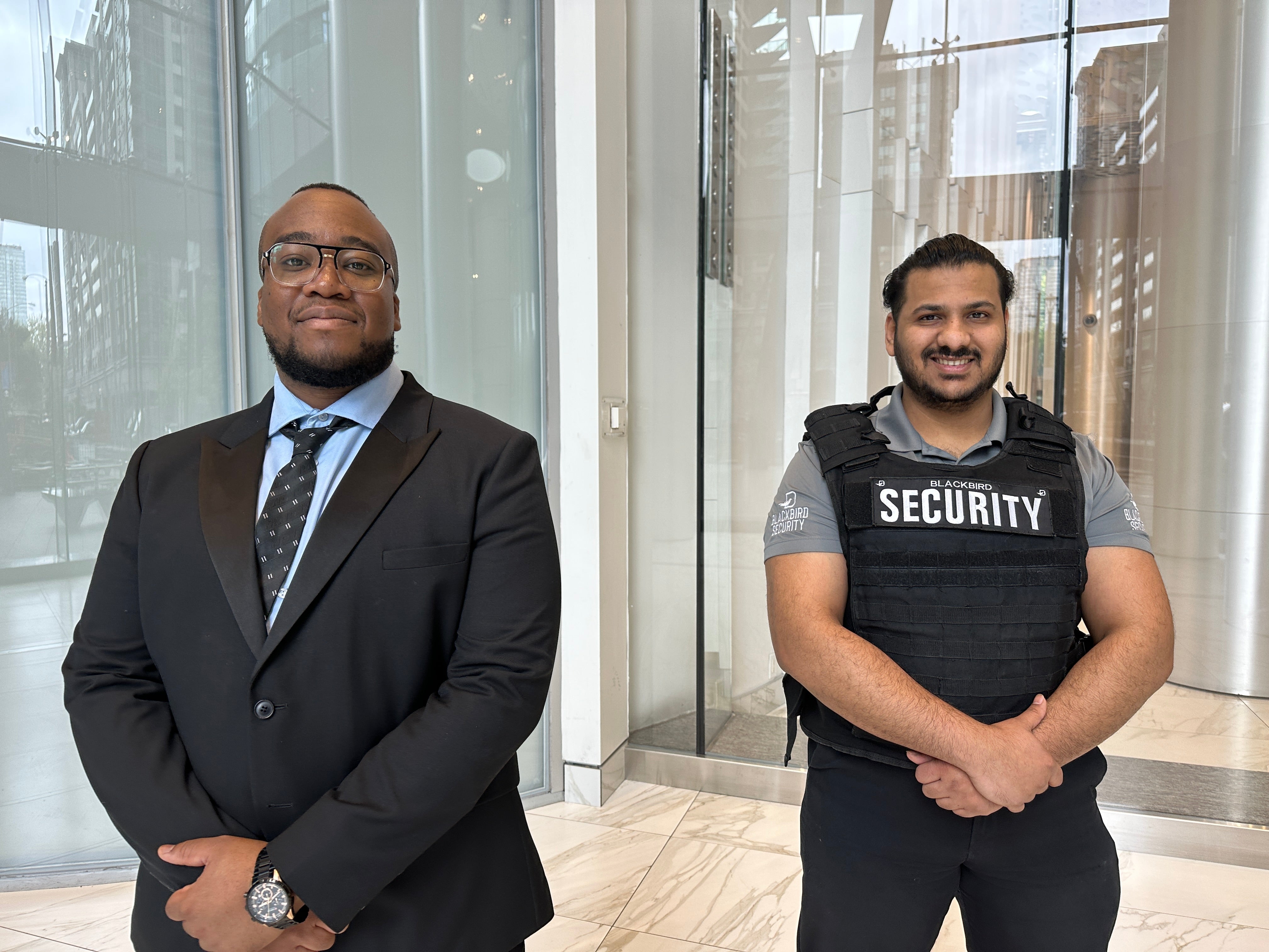 Uniformed Blackbird security guard and a suit and tie security guard stand in front of a condominium building entrance 