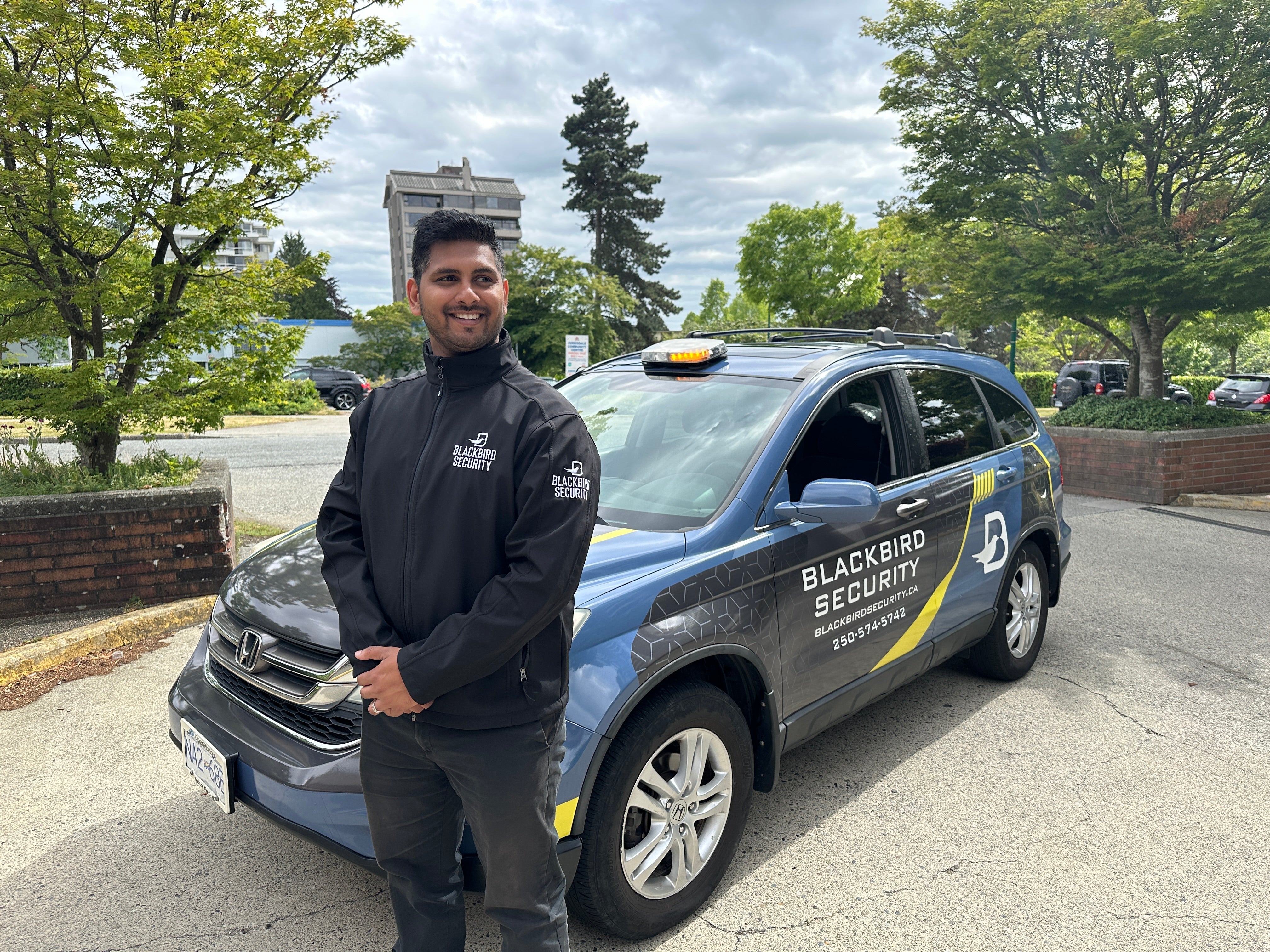 Uniformed Blackbird security guard in front of Mobile patrol car