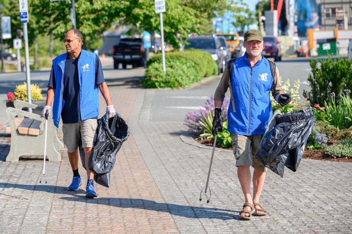 2 men carrying garbage bags and picking up trash