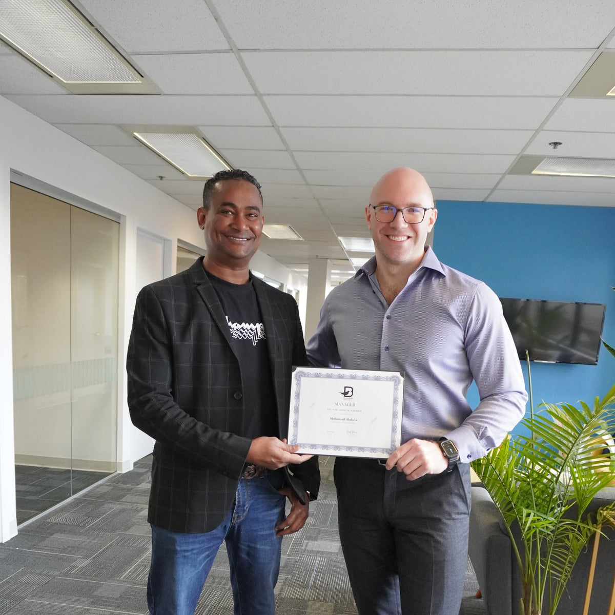 Two men standing together in office holding certificate