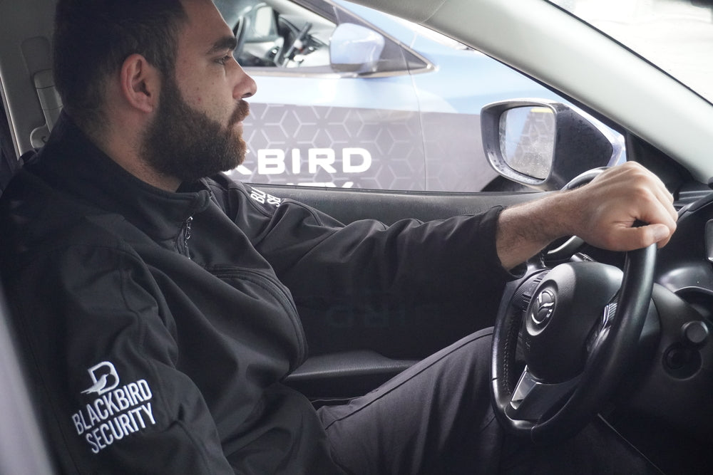 Person sitting in a car wearing a Blackbird Security jacket.