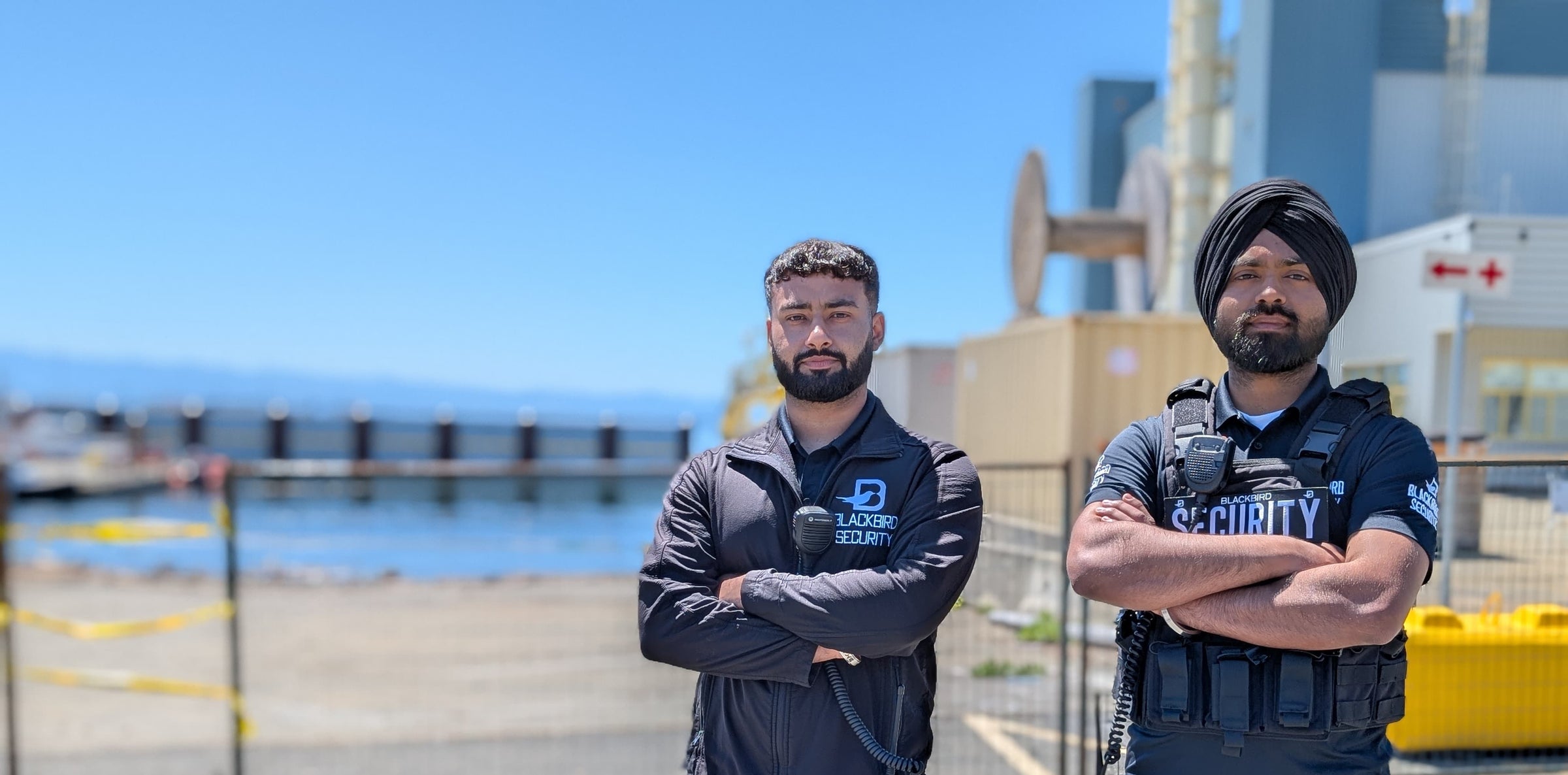 Two security personnel standing in front of a industrial area with clear blue sky.