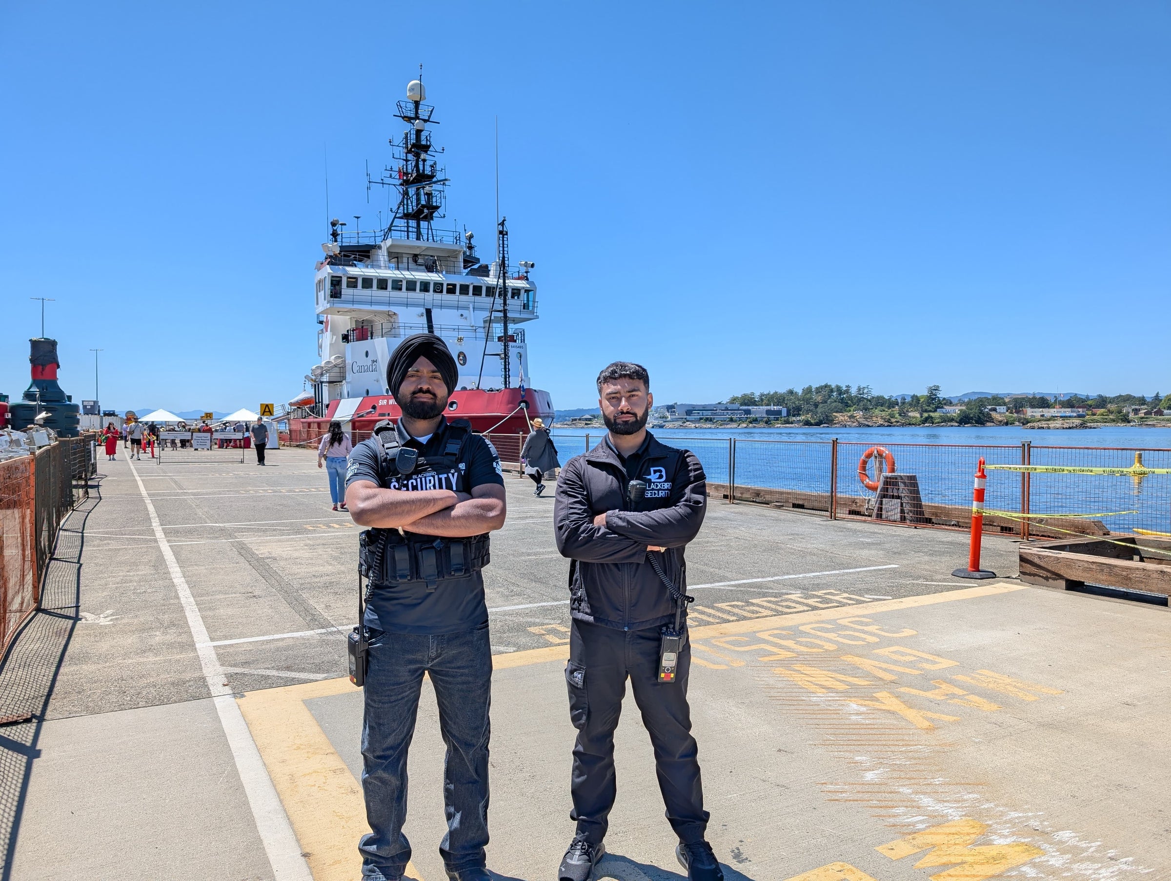 Two security guards in uniform standing on a dock with a large ship in the background.