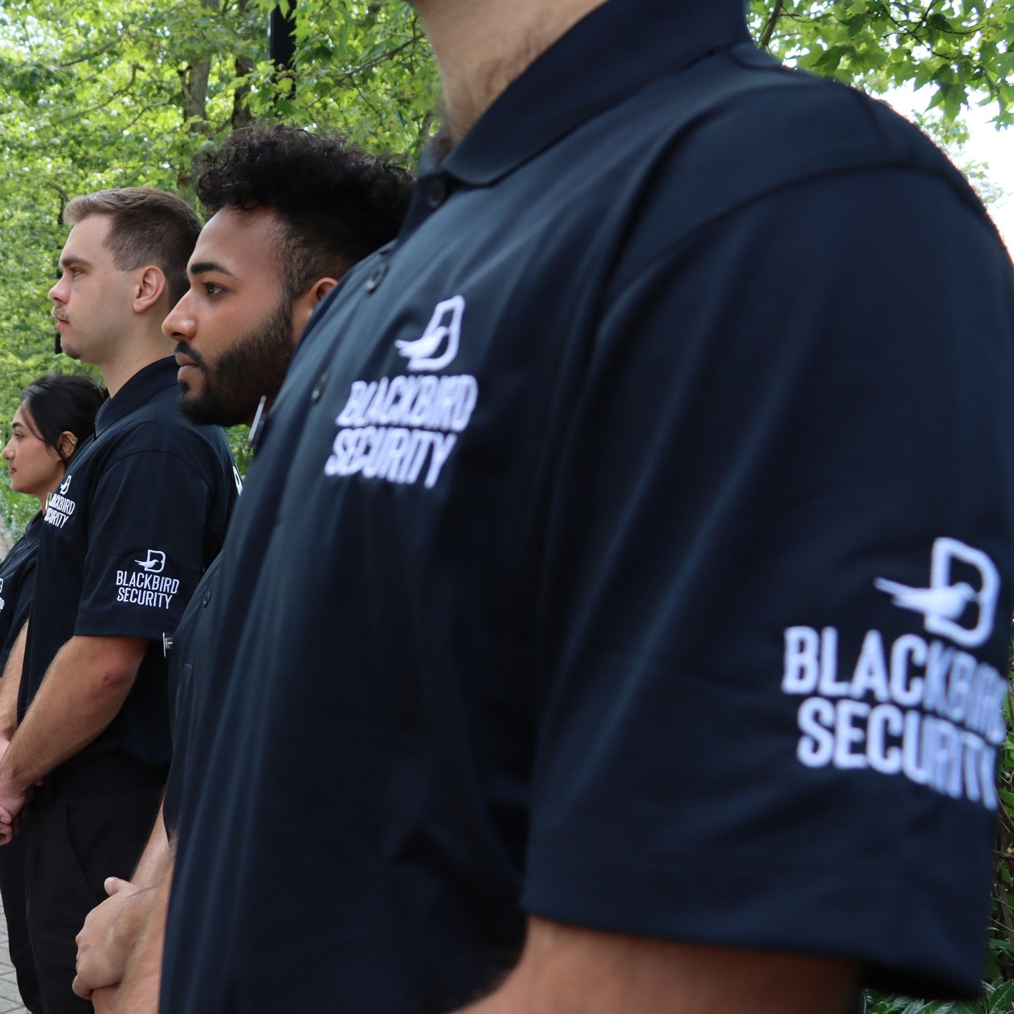 Four Blackbird security guards standing by trees