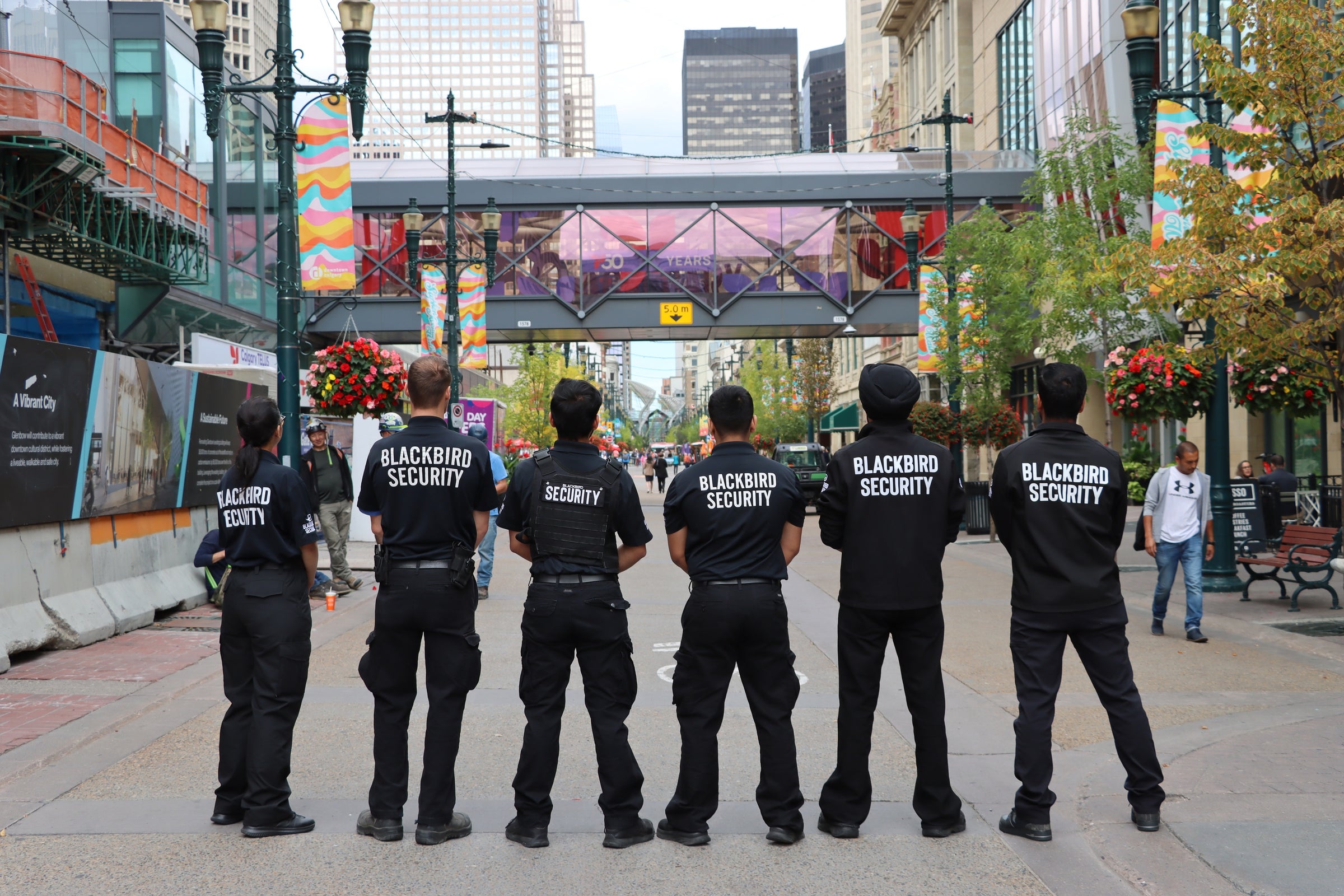 6 uniformed blackbird security guards looking up Granville street