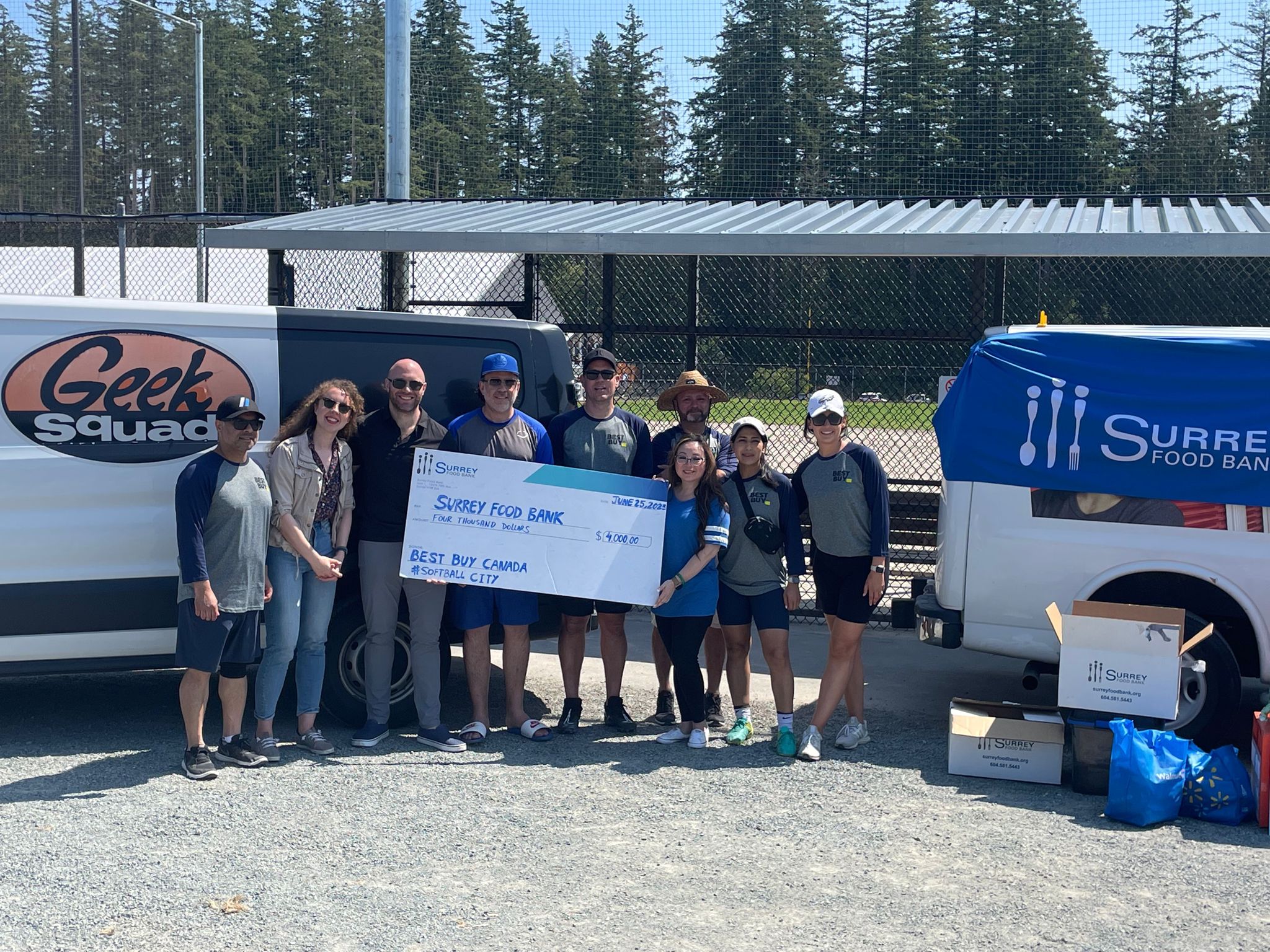 Group of people standing in front of baseball diamond with large cheque