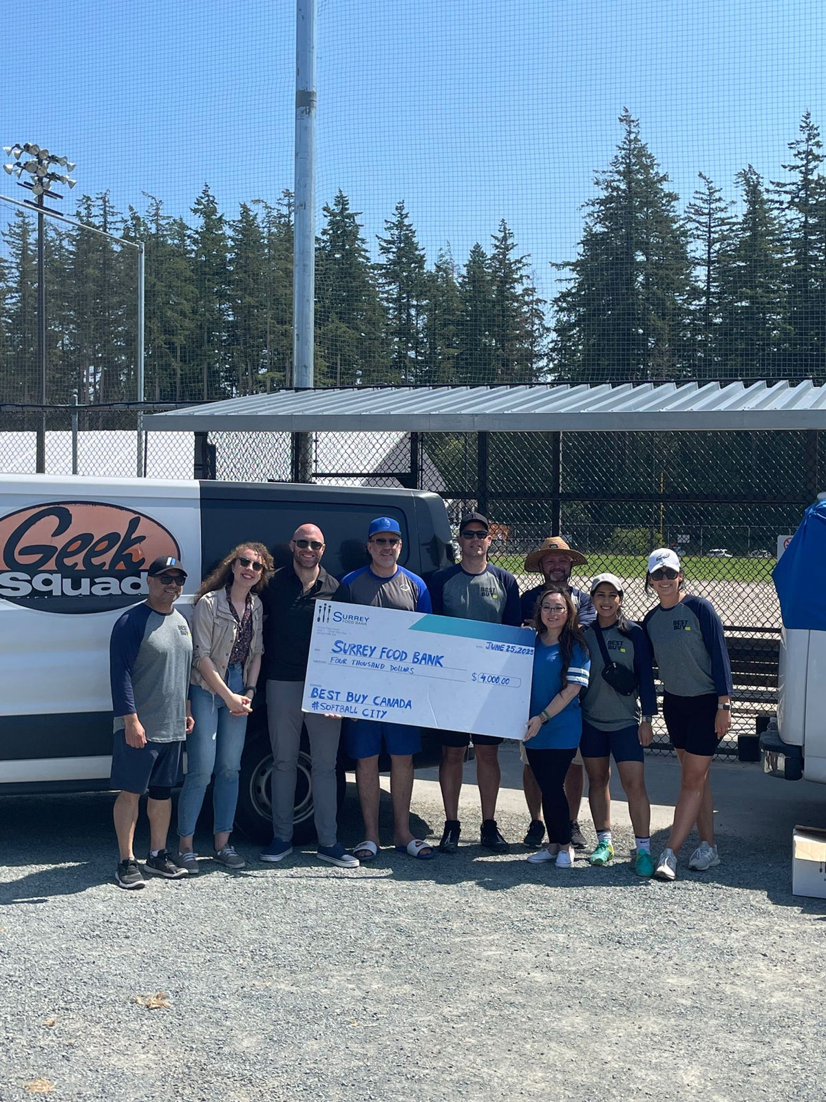 Group of people holding large cheque in front of baseball diamond