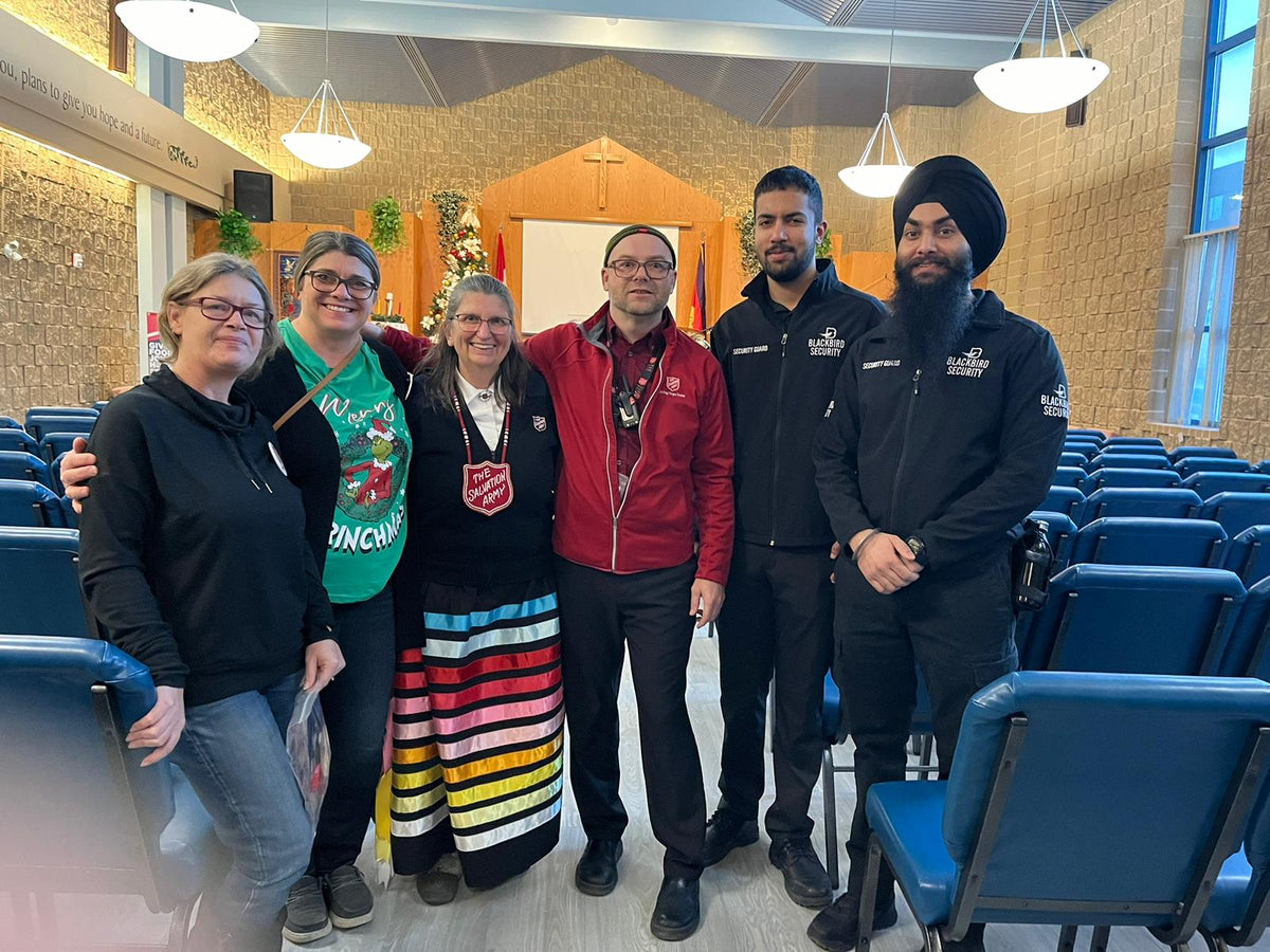 Two Uniformed Blackbird security guards standing in church with group of people from Salvation Army