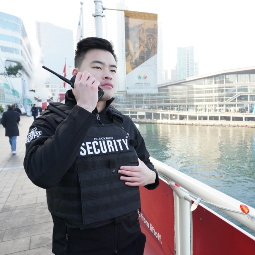 Blackbird security guard looking at Canada Place waterfront with radio in hand