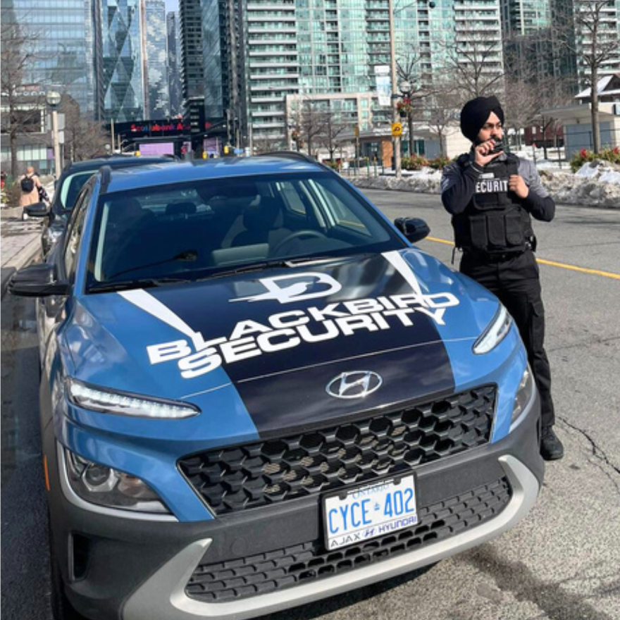 Uniformed Blackbird security guard in front of Mobile patrol car speaking on radio