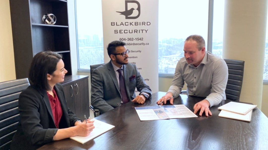 3 people sitting in meeting at board room table in office building with Blackbird Security banner in background