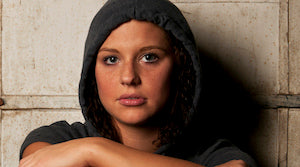 Young woman in hoodie sitting against a wall