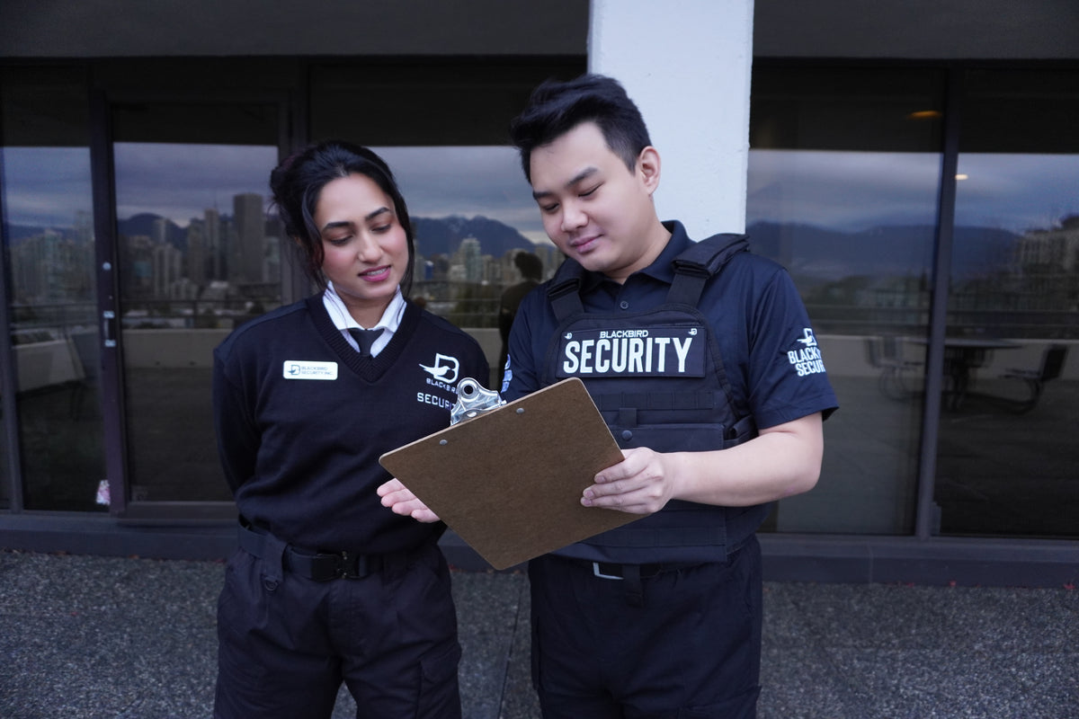 Two security personnel in uniform standing outdoors with a clipboard.