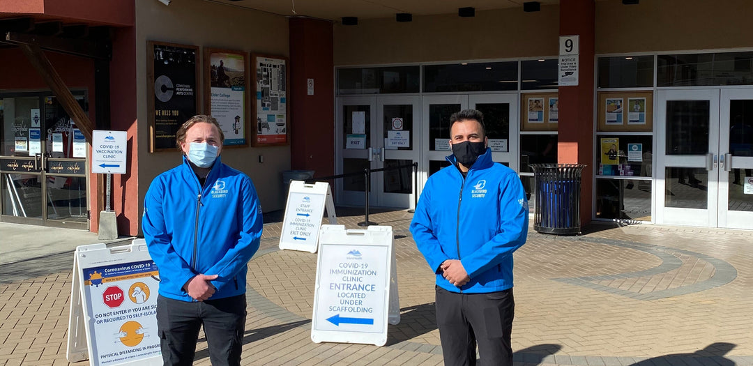 Two people in blue jackets standing outside a building with signs and arrows.
