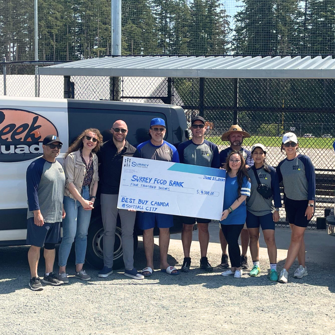 group of people holding large cheque in front of baseball field
