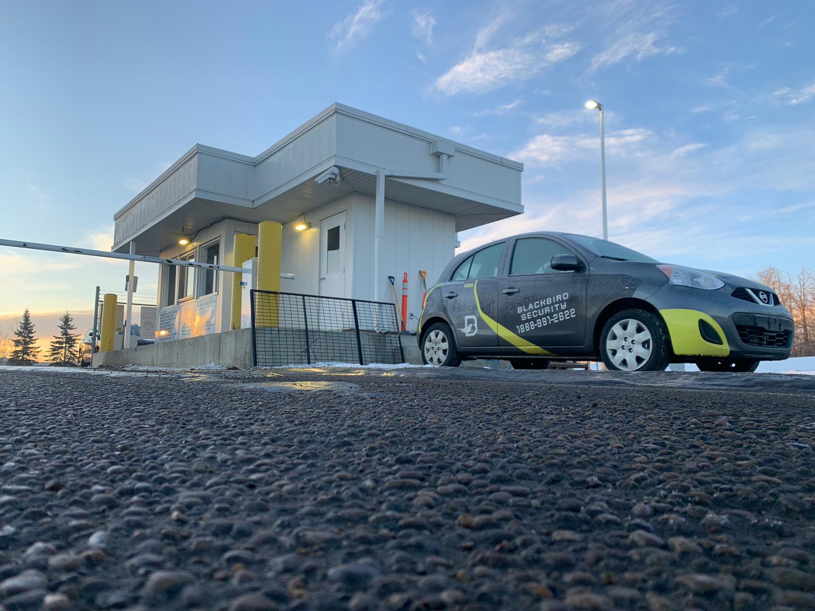 A Blackbird Security mobile patrol car parked near a security gatehouse